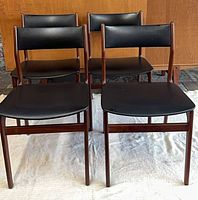 Front view of four matching teak chairs with black leather upholstery