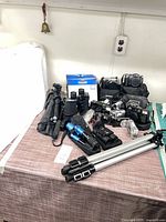 Group shot of entire lot on table showing tripods, cameras, binoculars, thermometer, accessories