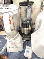 Two countertop blenders: Sunbeam white plastic base and Breville stainless steel base, both with clear jars and lids displayed on tabletop