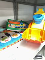 All three baby toys on shelf: yellow-blue vehicle, green musical toy, soft piano mat