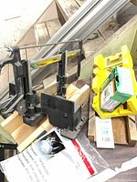 Overall lot showing jig with clamp, yellow accessory block, green fastener box, packaged respirator, and wood scraps