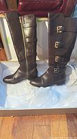 Full view of both brown leather knee-high boots standing in box