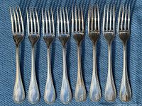 All eight Christofle Perles dessert forks laid side by side on blue fabric.