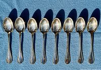 All eight Christofle Perles dessert spoons laid out bowl up on blue fabric