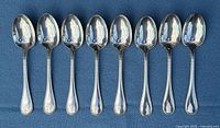 All eight Christofle Perles tablespoons lined up on blue background
