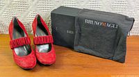 Pair of red suede pumps beside box and dust bag
