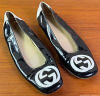 Top view of both flats showing black patent uppers, white GG logo toe appliqués, white counters