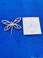 Front view of crystal butterfly brooch alongside booklet