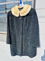 Full front view of black lambswool coat with cream fur collar hanging on hanger