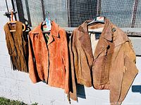 All three suede garments hanging: fringed vest, orange-tan jacket, brown Bermans jacket