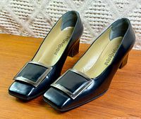 Pair of black YSL pumps three-quarter view showing leather, buckle, heels
