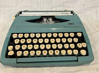 Front view of blue-aqua Smith-Corona Corsair Deluxe typewriter showing keys and type basket