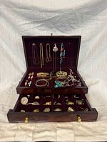 Overall view of open jewellery box showing necklaces hanging, bracelets, drawer with brooches