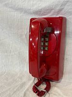 Front view of red wall-mounted telephone showing handset, keypad and cord