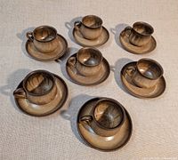 Full set of mugs and saucers arranged on cloth backdrop