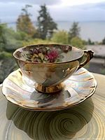 Side view of teacup on saucer showing floral interior, teal panels, luster glaze, gold trim