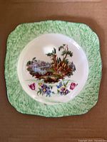 Front of plate showing green border, landscape scene, scalloped square shape