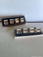 Two clear-lid boxes each holding four silver-tone napkin rings