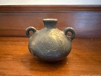 Front view of black pottery vase showing shape, handles, incised design