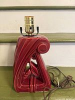 Full view of red glazed ceramic lamp base showing form, cord, and socket