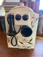 Front view showing telephone shape, black receiver and floral painting