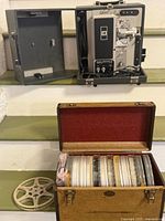 Projector with open case door and film reel case with contents