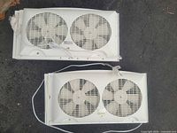 Two white twin window fans side by side on ground