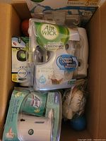 Box contents showing packaged Air Wick Freshmatic kit, Lysol No-Touch kit, car vent clip, loose dispensers and fragrance balls