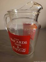 Left front angle of clear glass pitcher showing Bacardi rum & Coca-Cola graphic and pour spout