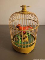 Front view of yellow plastic bird cage with red bird inside