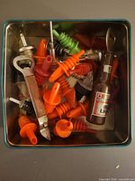 overview of tin containing assorted pour spouts and bottle openers