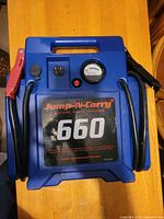 Front view of Jump-N-Carry 660 jump starter showing gauge, cables, clamps and label