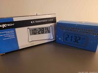 Two boxed digital alarm clocks: Nexxtech R/C Transparent Clock and Optically Controlled LCD Alarm Clock