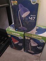Three boxed Globe EnerSaver desk lamps, colors visible on packaging