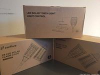 Three product boxes: two zanflare 99 LED Solar Flame Light 2-packs and one LED Solar Torch Light 2-pack