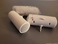 Two unwrapped white cylindrical mini speakers and one bubble-wrapped speaker