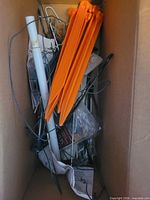 Box containing assorted orange plastic, metal, and white plastic stakes