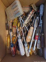 Box containing numerous screwdrivers and a plastic scraper