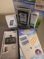 Multiple boxed thermometers including AcuRite, Voice Craft, refrigerator thermometer, hygrometer