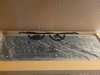 Keyboard inside box, covered with protective plastic, USB cable visible