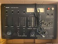 Front view of Numark DM-1550 mixer in box showing overall layout, VU meters, sliders, knobs and power cord