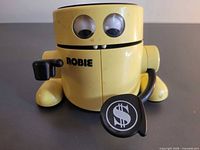 Front view showing Robie robot piggy bank with eyes, logo, and coin scoop