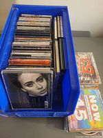 Blue bin filled with stacked CDs; Adele 25 cover and Now 53 visible