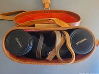 Overhead view inside open leather case showing binoculars and lens caps