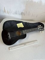 Full view of black soprano ukulele with ruler and gig bag