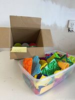 Cardboard box with Play-Doh cans next to clear bin of cutters and molds