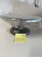 Side view of the metal rotating cake stand wrapped in plastic on pedestal base