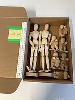 Box containing 2 large and 6 medium wooden articulated figures next to ruler