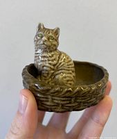 Front angle of porcelain cat in basket figurine held by hand