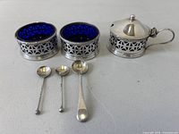 Front view of two salts, mustard pot with lid, and three spoons